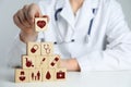 Doctor building pyramid of wooden cubes with different icons at white table, closeup. Insurance concept Royalty Free Stock Photo
