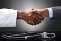 Doctor And Business Man Shaking Hands With Stethoscope On Desk