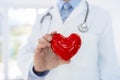 Doctor or cardiologist holding heart with care in hands at hospital office