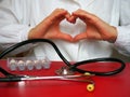 Doctor cardiologist with a stethoscope shows the heart with his hands. Stethoscope and medicines on the table. Hands gesture. Royalty Free Stock Photo