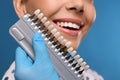 Doctor checking young woman`s teeth color on blue background, closeup. Cosmetic dentistry