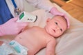 Doctor checks the temperature of the newborn baby with a thermometer. A nurse in uniform measures the child fever with a Royalty Free Stock Photo