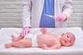 Doctor checks the temperature of the newborn baby with a thermometer. A nurse in uniform measures the child fever with a