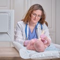 Doctor checks the throat of a newborn child with a plowshare. A nurse in uniform with a wooden stick in her hand examines the Royalty Free Stock Photo