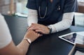 A doctor and a comforter. an unrecognizable doctor holding hands with a patient in an office.