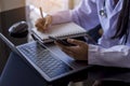 Doctor woman using mobile smart phone and writing something on notebook, work on laptop computer Royalty Free Stock Photo