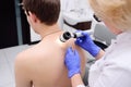 The doctor dermatologist examines birthmarks and birthmarks of the patient with a dermatoscope