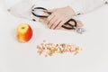 Doctor at desk with handful pills, apple in office in hospital. Woman holds in hands stethoscope in consulting room Royalty Free Stock Photo