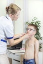 Doctor in a doctor`s office while medical examining the tonsils of a boy with glasses.