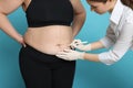 Doctor drawing marks on obese woman`s body against light blue background, closeup. Weight loss surgery