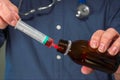 A doctor drawing medicine from a bottle into a syringe prior to administering it to a patient.