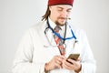 A doctor with dreadlocks and a beard is holding a smartphone in his hands, a stethoscope and a badge are hanging around his neck Royalty Free Stock Photo