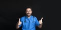 A doctor dressed in a blue hospital uniform smiling and raising his two thumbs up indicating that all is well Royalty Free Stock Photo