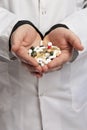 A doctor in a dressing gown holds a handful of multicolored pills and capsules in his hands. Pharmacology and Medicine. Vertical