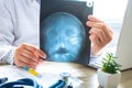 Doctor examines x-ray scan of head and skull near computer during work and patient advice in office. Diagnostics of diseases of e Royalty Free Stock Photo