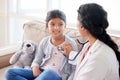 Doctor examining a little girl with stethoscope. Female paediatrician listening to childs heartbeat during home visit or