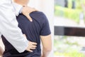 Doctor Examining Sore Back Muscles of Young Man Sitting Shirtless and Slumped Over on Table