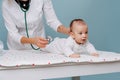 Doctor exams baby with stethoscope on a special table over blue background Royalty Free Stock Photo