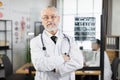 Doctor in eyewear and lab coat keeping arms crossed indoors Royalty Free Stock Photo