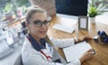 Doctor fill in patients medical history, stethoscope on neck, modern clinic office