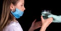 A doctor gives a cute little girl a glass of water. On the girl`s face there is a mask to protect against Covid-19