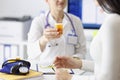 Doctor giving jar of medicines to young woman in clinic closeup