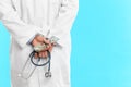 Doctor in handcuffs with bribe and stethoscope on light blue background, closeup. Corrupted medicine Royalty Free Stock Photo