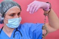 Doctor hands in handcuffs on red background, closeup. Woman hands in pink medical gloves handcuffed, coronavirus quarantine