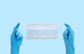 Doctor hands in medical gloves holding surgical face mask on blue. Coronavirus protection concept