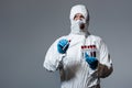 Doctor in hazmat suit, medical mask and goggles holding test tube with coronavirus lettering isolated on grey