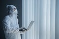 Doctor in hazmat suit works with laptop