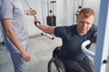 Doctor helps young wheelchair man pulls resistance band with arm