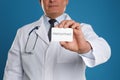 Doctor holding business card with word HEMORRHOID on blue background