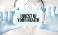 Doctor holding card in hands and pointing the word INVEST IN YOUR HEALTH Royalty Free Stock Photo