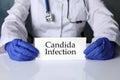 Doctor holding card with phrase Candida Infection at white table, closeup