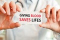 Doctor holding a card with text GIVING BLOOD SAVES LIFES, medical concept Royalty Free Stock Photo