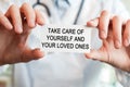 Doctor holding a card with text TAKE CARE OF YOURSELF AND YOUR LOVED ONES