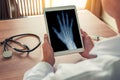 Doctor holding a digital tablet with x-ray of a right hand. Stethoscope and syringe on the desk. Osteoarthritis concept