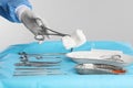 Doctor holding forceps with tissue over surgical instruments on table against light background, closeup Royalty Free Stock Photo