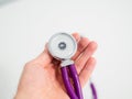 Doctor holding in hand round detail of purple stethoscope on white background. Close-up