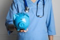 Doctor holding light blue ceramic piggy bank against white wall, closeup. Medical insurance Royalty Free Stock Photo