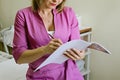 Doctor holding a notebook in his hand. Close up of female beautician in pink uniform filling out a medical form