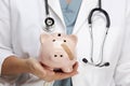 Doctor Holding Piggy Bank with Bandage on Face Royalty Free Stock Photo