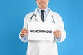 Doctor holding sign with word HEMORRHOID on background, closeup