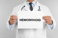 Doctor holding sign with word HEMORRHOID on grey background, closeup