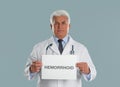 Doctor holding sign with word HEMORRHOID on grey background