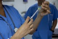 Doctor holding a syringe in a hospital room in the background another doctor observing