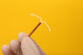 Doctor holding T-shaped intrauterine birth control device on yellow background, closeup