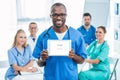 handsome smiling african american doctor holding tablet with colleagues sitting at table