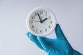 Doctor holding white alarm clock in hand with glove